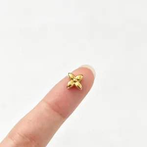 Close-up of a small gold four-leaf flower stainless steel bead on a finger for scale.