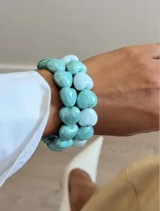 Close-up of mint green and turquoise heart-shaped beaded bracelets on wrist.