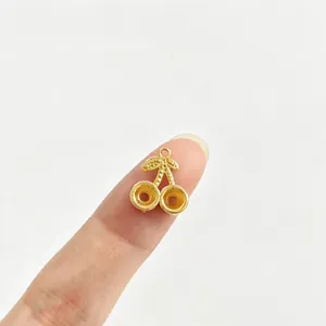 Detailaufnahme eines goldenen Kirsch-Anhängers auf einem Finger zum Größenvergleich