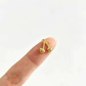 Nahaufnahme eines winzigen goldenen Kirschherz-Anhängers auf einem Finger als Maßstab.