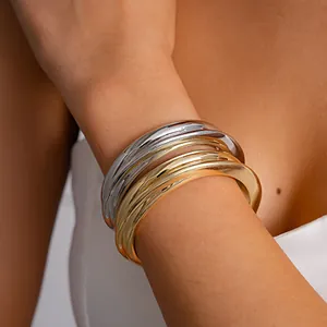 Macro detail of minimalist stacked gold and silver metallic open bangles on a woman's wrist