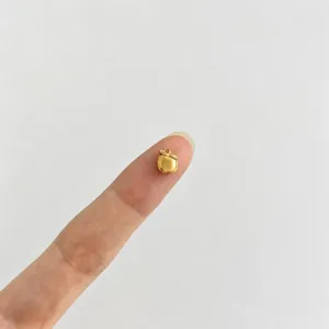 Détail d'un mini pendentif pomme en or 18 carats posé sur un bout de doigt pour l'échelle.