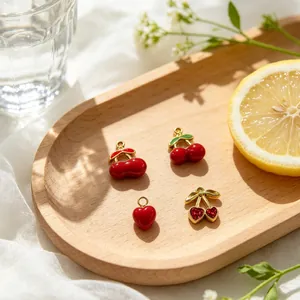 Detalle de colgantes de cereza y corazón esmaltados para joyería DIY en bandeja madera