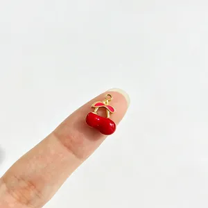Primer plano de un pequeño colgante de cereza roja esmaltada en un dedo para la escala