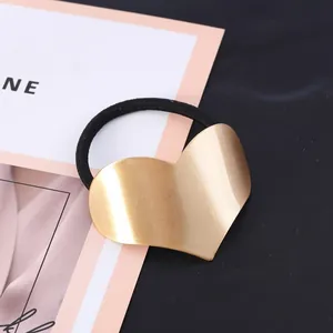 Close-up of gold brushed heart hair tie showing metallic texture and black elastic band.