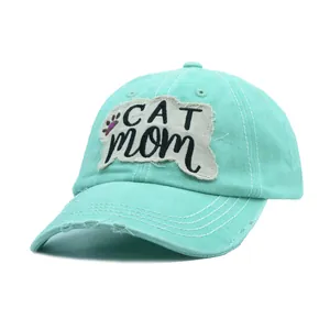 Κοντινό πλάνο του κεντημένου σήματος 'Cat Mom' σε ένα ξεβαμμένο πράσινο καπέλο μπέιζμπολ