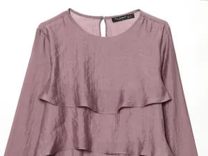 Dettaglio di una maglia color malva con volant a strati e maniche lunghe.