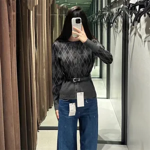 Detail of a grey argyle knit cardigan with a black belt in a fitting room context.