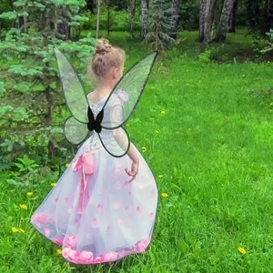 Young girl wearing butterfly fairy wings and petal princess dress in a green forest meadow