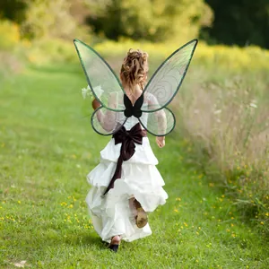 Back view of a girl in a white dress wearing green translucent butterfly fairy wings in a field