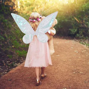 Little girl wearing iridescent butterfly fairy wings walking through a sunny green forest
