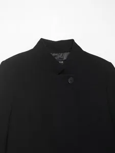 Dettaglio di un blazer corto nero da donna con colletto alla coreana e bottone.
