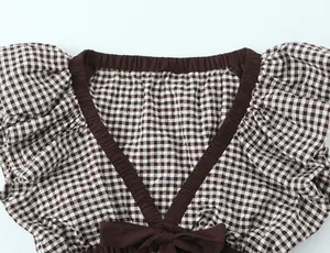 Detalle del escote en V de blusa de cuadros marrones con lazo y borde elástico.