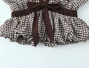 Detalle de una blusa de cuadros marrones estilo globo con un lazo grande y cintura elástica