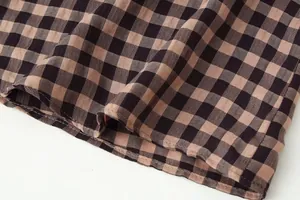 Close-up detail of the brown and black gingham fabric texture and hem of the skirt.