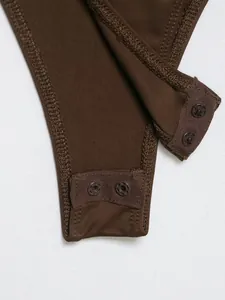 Close-up detail of the snap button closure at the crotch of a brown bodysuit garment.