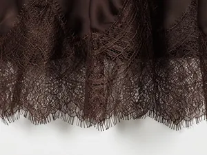 Close-up of delicate lace trim on a dark brown satin midi skirt with eyelash edges.