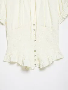 Vista detallada de una blusa fruncida crema con botones de perlas y dobladillo volante