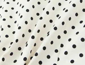 Detalle macro de tela blanca con patrón clásico de lunares negros para conjunto.