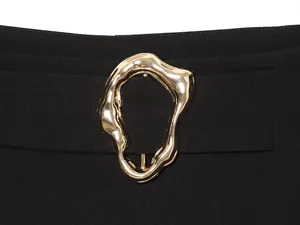 Macro view of an irregular gold-finished metal buckle on black fashion trousers.