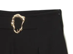 Close-up of black casual barrel pants featuring an irregular gold buckle and side zipper.
