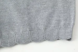 Macro view of the grey knitted fabric texture and scalloped hem on a stylish women's cardigan