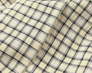 Close-up of yellow and black plaid fabric with seersucker texture and neat overlock stitching.