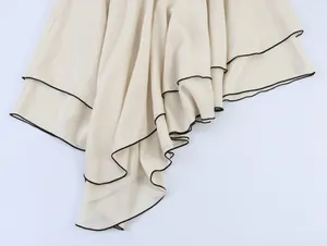 Close-up showing the draped layered fabric and black piping of the asymmetric hem