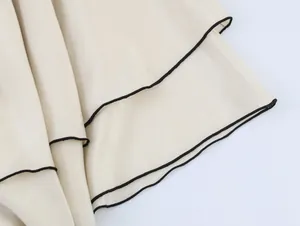 Close-up detail of cream asymmetrical skirt with black contrast piping on the layered hemline