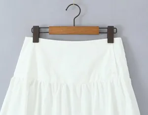 Close-up of a white mini A-line skirt featuring side button details and a pleated hem