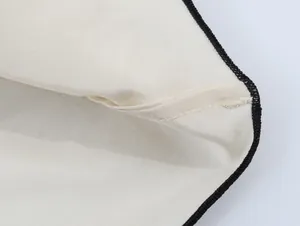 Detailed macro view of black contrast edge stitching on a cream asymmetric skirt fabric.