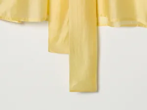 Close-up detail van de gladde textuur van gele satijnstof op een elegante strikblouse
