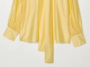 Detailopname van de gele satijnen blouse met strik en geplooide manchetten
