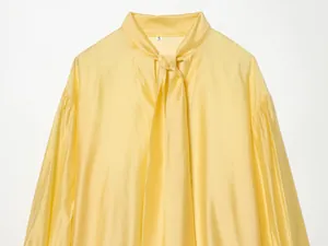 Detailweergave van een gele satijnen blouse met een elegante strikhals-lijn ontwerp.