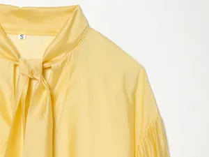Gedetailleerd overzicht van de elegante satijnen stof en de strikhals van een gele blouse