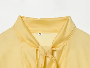 Detailweergave van de gele satijnen blouse met strikkraag en maateenheid-label