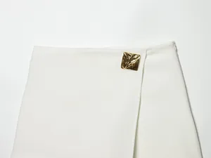 Detailed view of a white asymmetrical skort featuring a stylish gold square metal ornament.