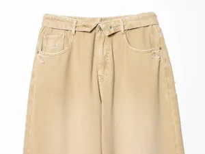 Détail de la taille repliée et des poches usées sur un jean en denim de couleur sable.