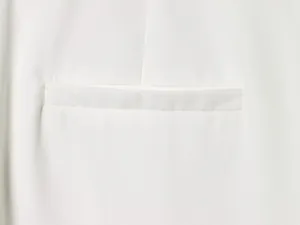 High-quality close-up showing the precise stitching and welt pocket of a white formal blazer