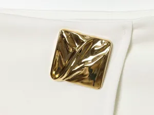 Close-up of the stylish gold metallic decorative patch on white asymmetric skirt pants.