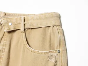 Gros plan d'un jean en denim kaki montrant la taille repliée et le détail de la poche