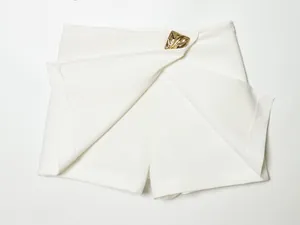 Detailed view of stylish white asymmetrical skort featuring a decorative gold buckle
