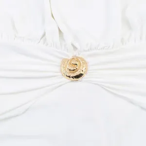 Macro view of a golden textured spiral metal buckle on a white pleated halter dress