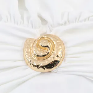 Detailed macro view of a golden spiral shell buckle on a white pleated halter neck dress