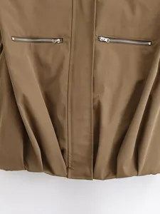 Detailed view of a brown puffy fashion vest showing silver zippers and elastic hemline