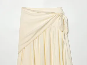 Close-up detail of a cream-colored wrap midi skirt featuring lace trim and elegant side-tie bow