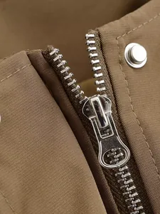 Close-up detail of silver metal zipper and snap button on khaki utilitarian garment.