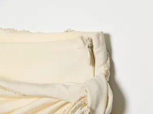 Detailed close-up of invisible side zipper and lace trim on a cream-colored midi skirt.