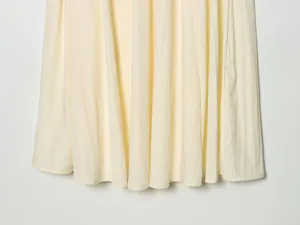 Close-up of light yellow pleated midi skirt showing fabric texture and hem detail