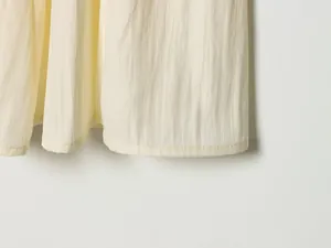 Detail shot of the crinkled fabric texture and hemline of a yellow midi skirt